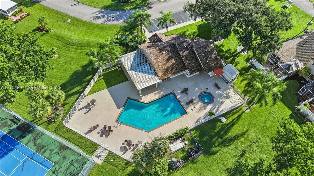 Aerial perspective of a property featuring an expansive paved patio, an in-ground swimming pool, a dedicated spa, a covered pergola, and a perimeter fence