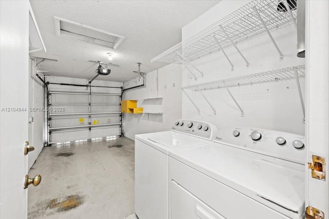 Enclosed garage featuring an automatic door opener, overhead lighting, wire shelving, and built-in laundry hookups