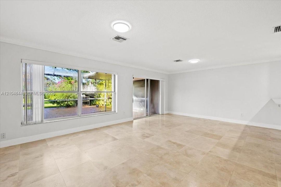 Spacious interior featuring large-format stone flooring, crown molding, expansive windows, and a sliding glass door providing natural light