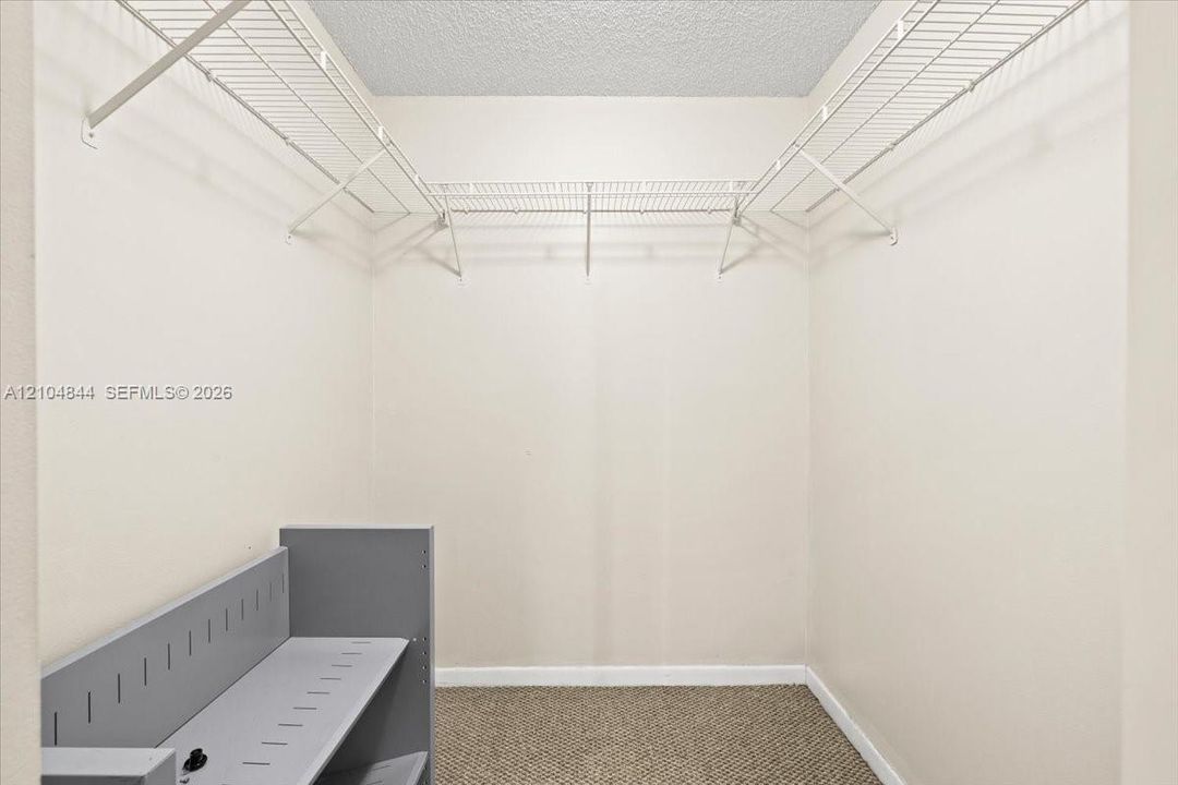 Walk-in closet featuring white wire shelving, neutral carpeting, and a built-in grey organizational unit