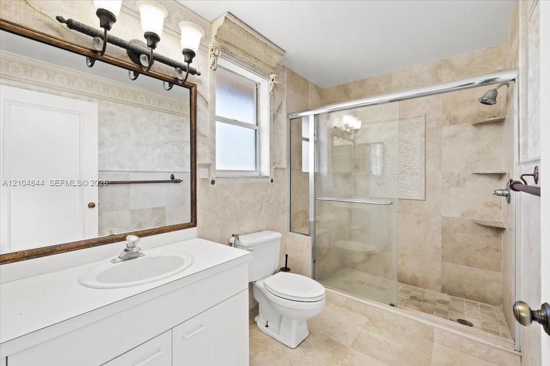 Bathroom featuring floor-to-ceiling stone tile, a glass-enclosed walk-in shower with integrated shelving, a white vanity with a solid-surface countertop, and a decorative crown molding accent