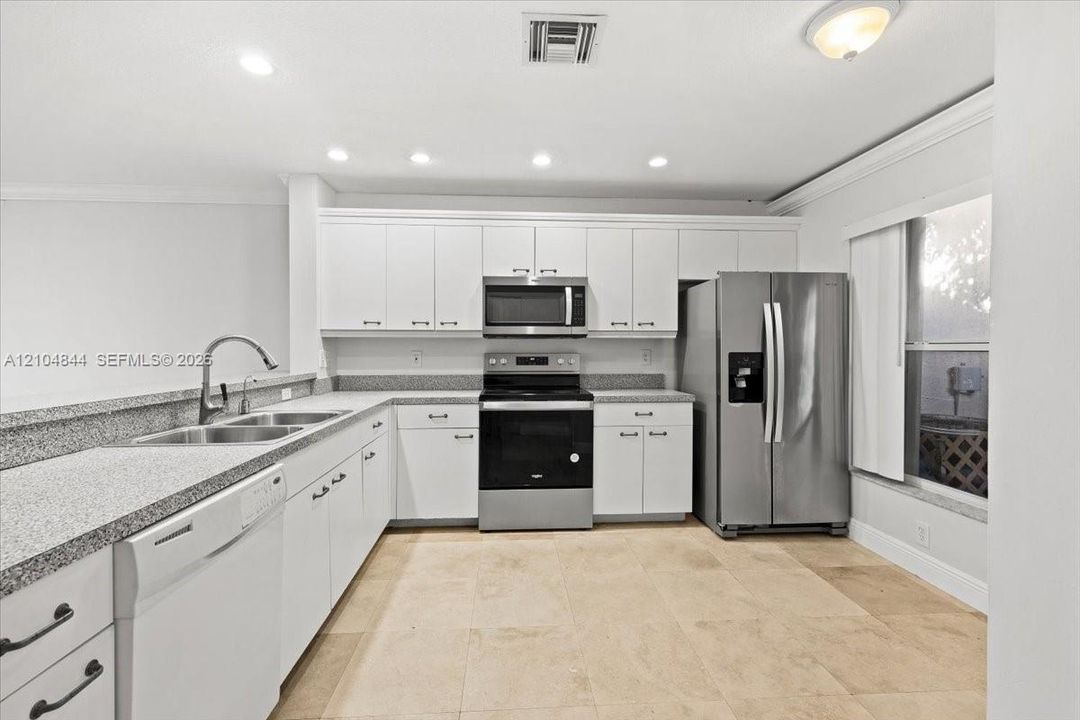 Kitchen featuring white cabinetry, speckled stone countertops, stainless steel appliances, a dual-basin undermount sink with a gooseneck faucet, and tile flooring