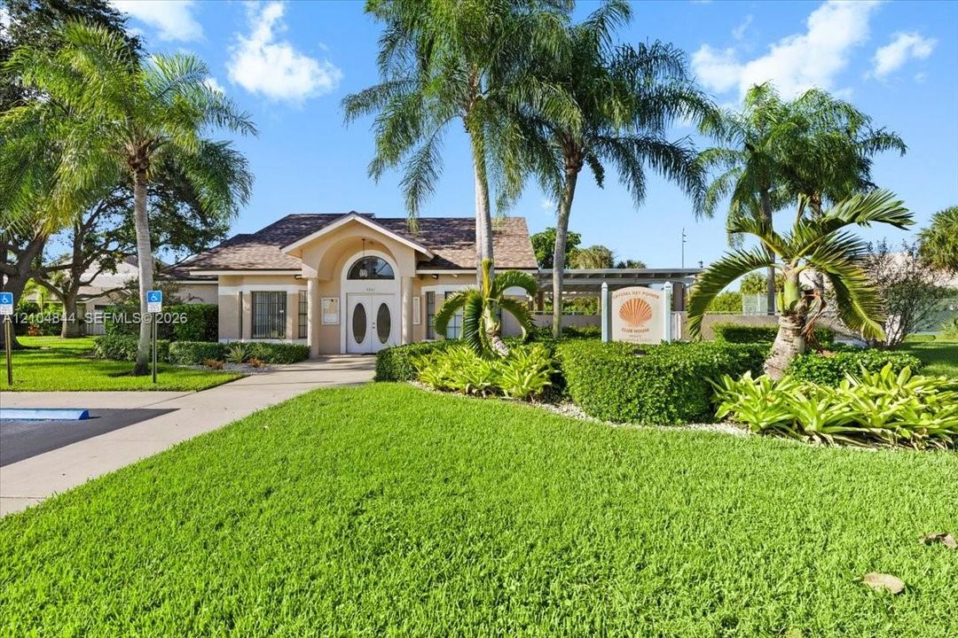 Stucco exterior with an arched entryway, double-door entrance, asphalt shingle roofing, manicured lawn, and mature palm trees