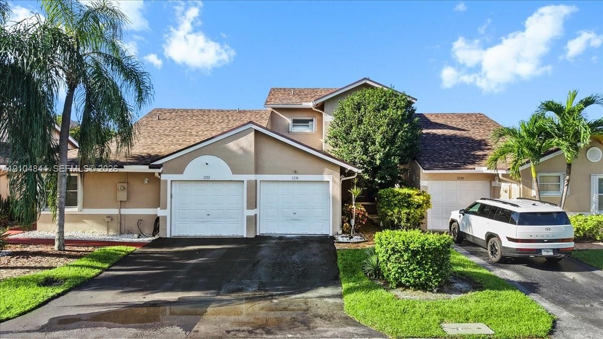 Multi-unit residential exterior featuring a multi-gabled roofline, dual-garage configuration, textured stucco facade, and established landscaping