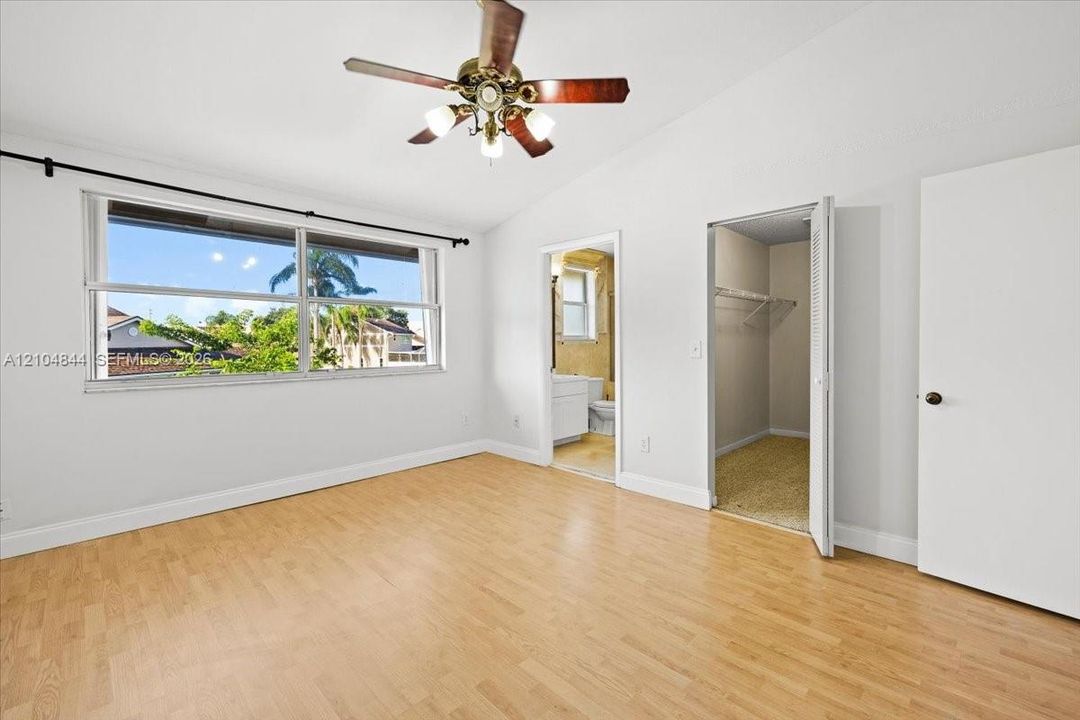 Bedroom featuring wood-finish flooring, vaulted ceiling, large multi-pane window, ceiling fan with light fixture, and closet with built-in shelving