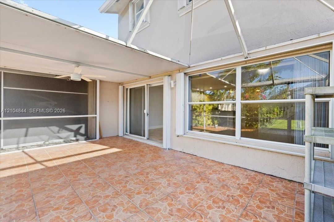 Screened-in patio featuring patterned ceramic tile flooring, a covered ceiling with an integrated fan, and oversized sliding glass doors