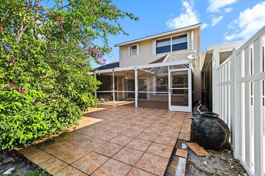 Rear exterior featuring a tiled patio and a covered, screen-enclosed porch area protected by a white vinyl privacy fence
