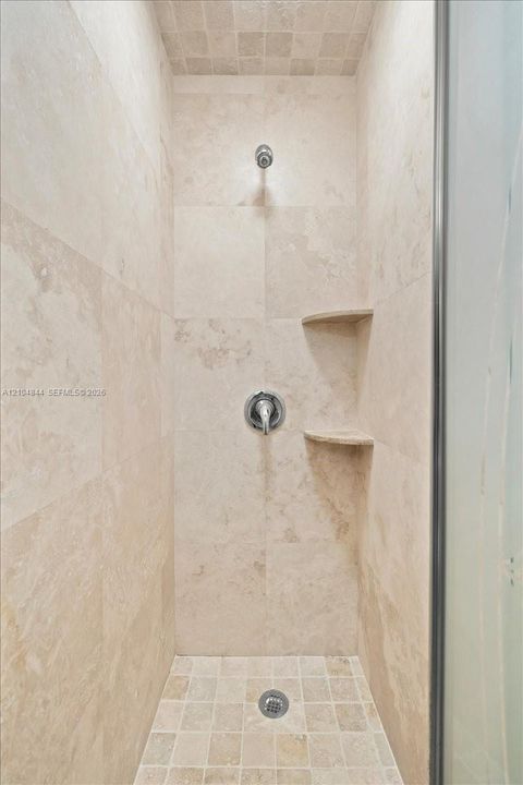 Shower stall featuring stone wall tiling, mosaic floor tile, built-in dual corner shelves, and a wall-mounted chrome fixture