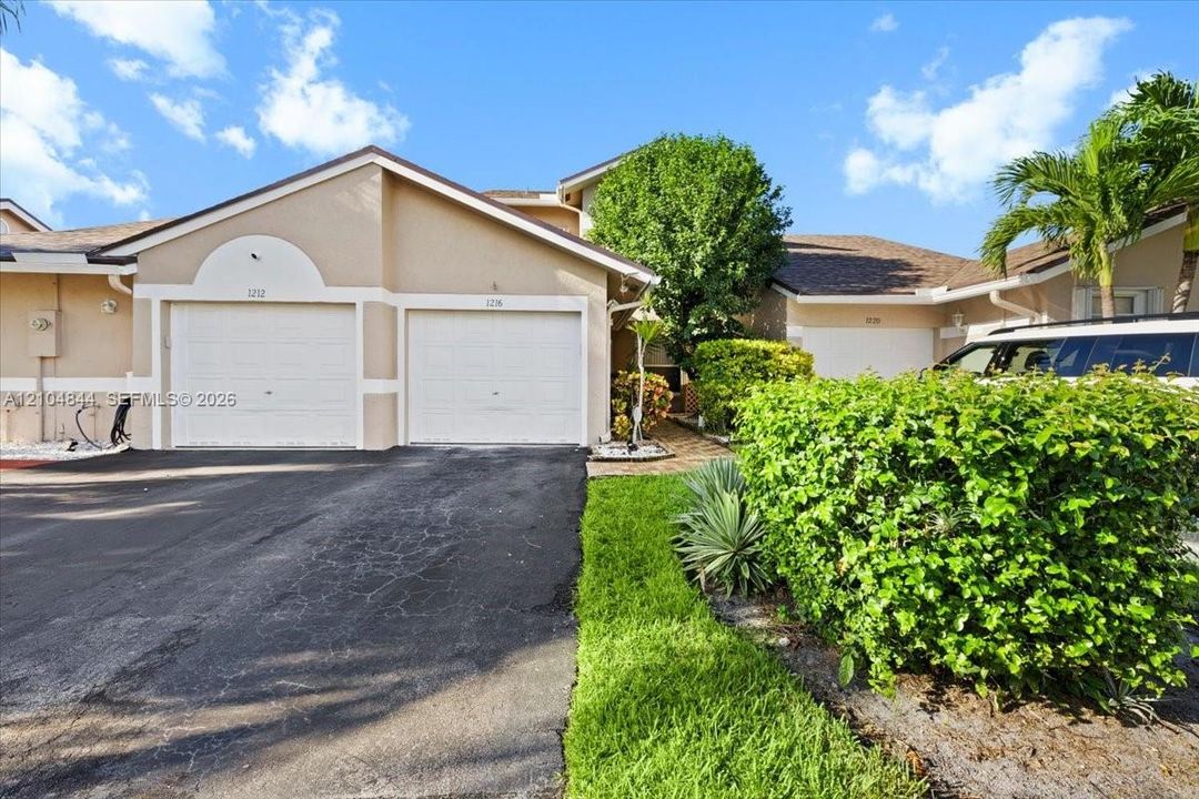 Stucco exterior featuring dual attached garage bays, arched architectural detailing, and landscaped grounds with mature palm trees
