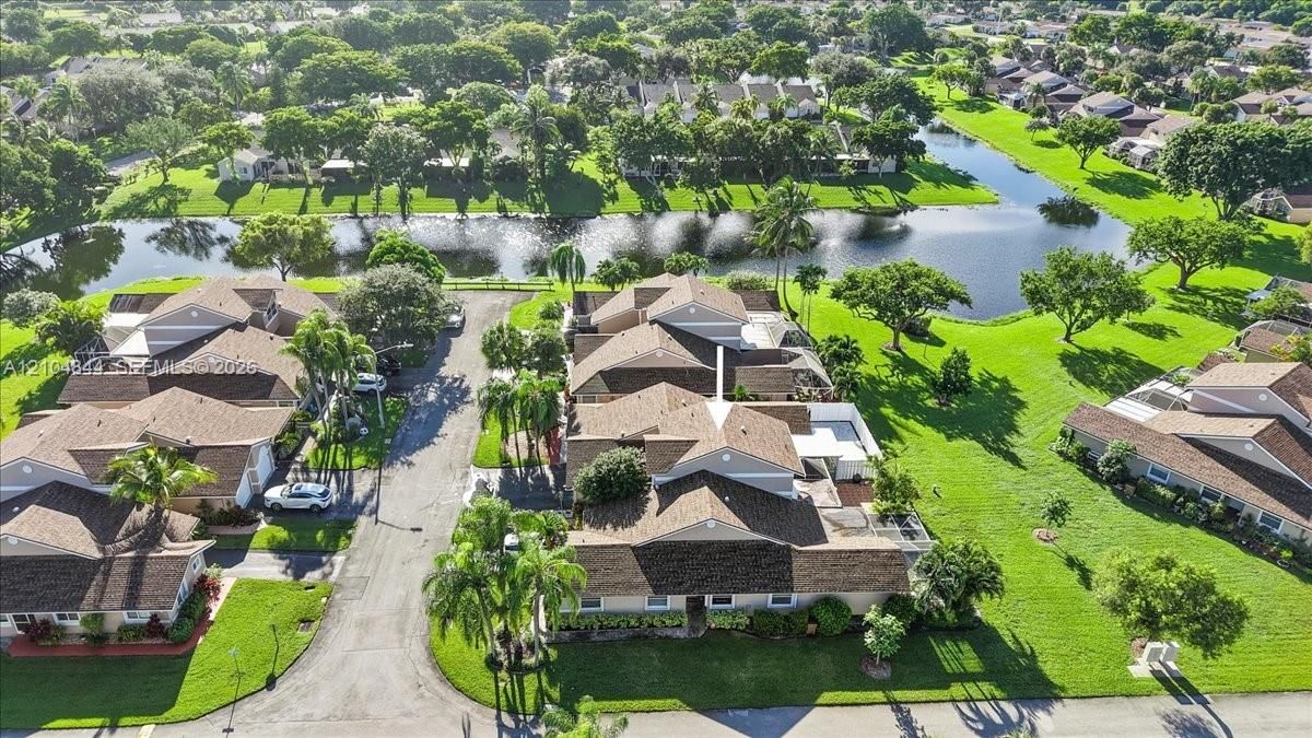 Aerial perspective of a multi-unit property featuring a shingle roof, paved access road, manicured lawn, and proximity to a water feature