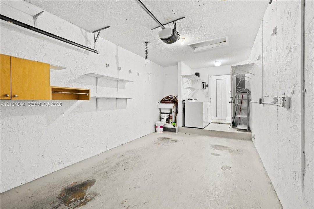 Garage featuring a concrete floor, built-in wooden wall cabinetry, fixed shelving units, utility sink, and a pedestrian door
