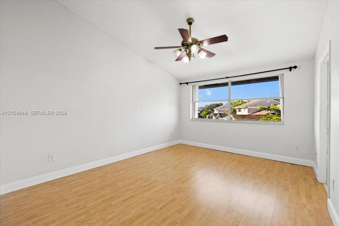 Room featuring vaulted ceilings, wood-finish flooring, a multi-blade ceiling fan with integrated lighting, and a horizontal window