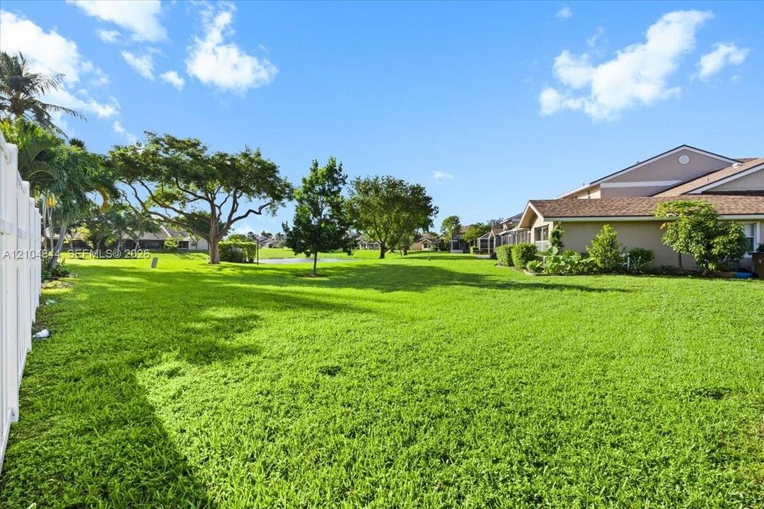 Expansive backyard featuring a sprawling lawn, mature trees, white vinyl privacy fencing, and exterior stucco siding with shingle roofing