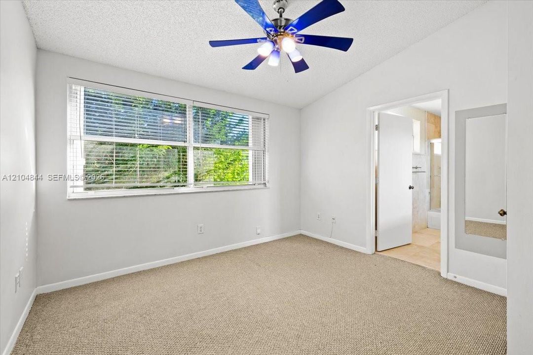 Neutral-toned carpeting, multi-pane window with horizontal blinds, ceiling fan with integrated lighting, and inset wall-mounted mirror