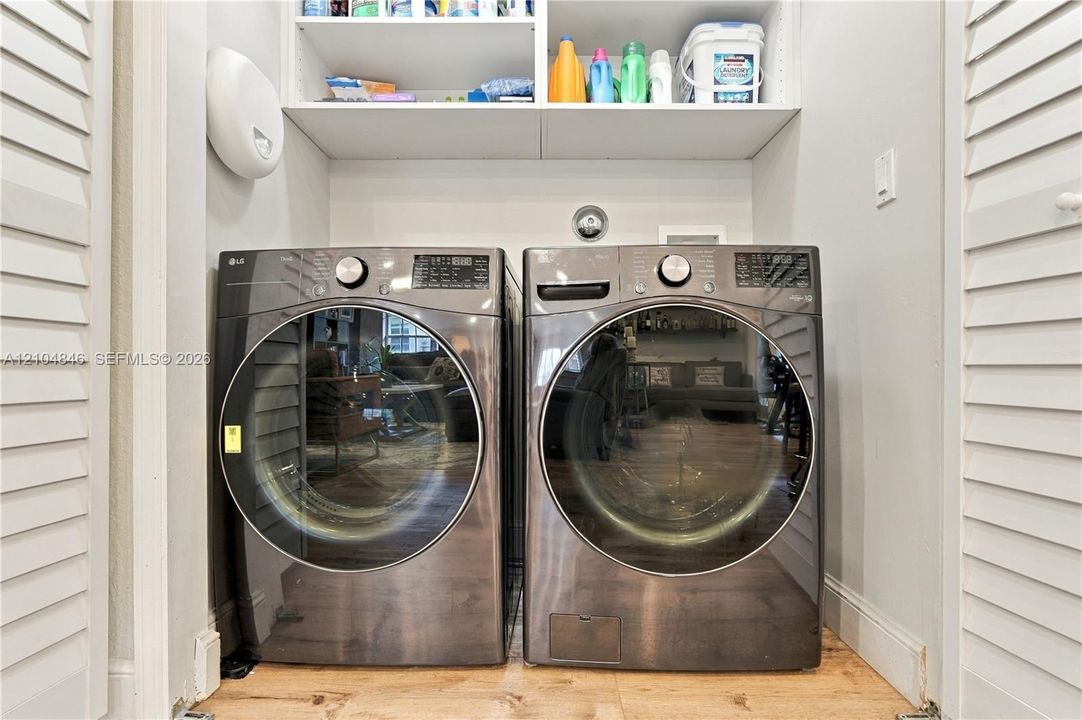 Laundry closet featuring high-capacity front-loading appliances, louvered bi-fold doors, and integrated overhead shelving