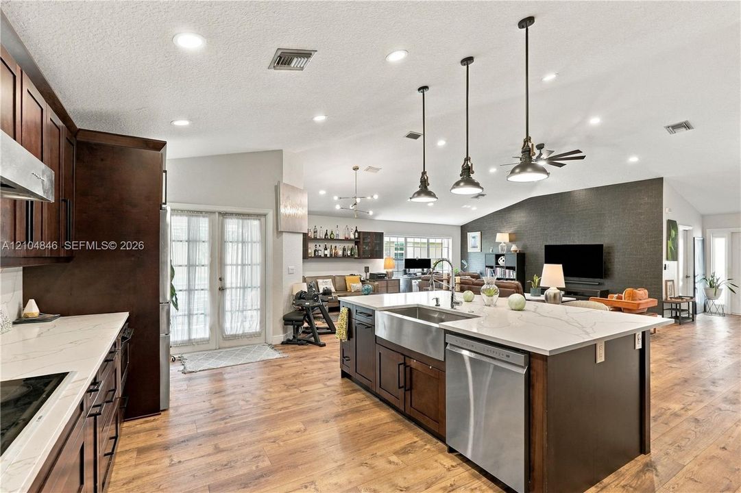 Kitchen featuring a large island with a stainless steel farmhouse sink and quartz countertops, dark wood-finish cabinetry, recessed lighting, and wood-finish flooring