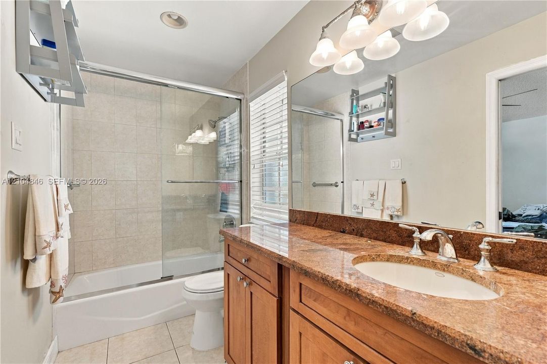 Bathroom featuring a stone-finish countertop with an integrated basin, wood-finish cabinetry, a large wall-mounted mirror, and a tub-shower combination with sliding glass doors