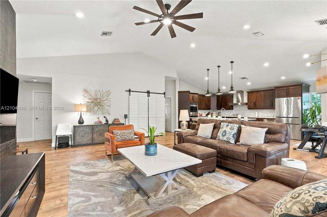 Vaulted ceilings, wood-finish flooring, recessed lighting, ceiling fan, and sliding barn door