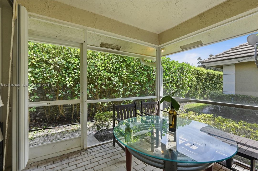 Screened-in patio featuring brick paver flooring, white structural framing, and perimeter landscaping