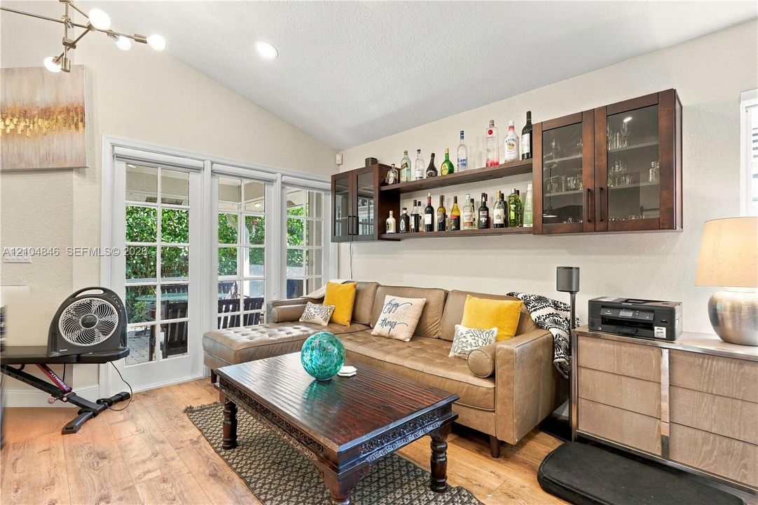 Vaulted ceiling, wood-finish flooring, multi-panel glass exterior doors, and dark wood built-in wall cabinetry
