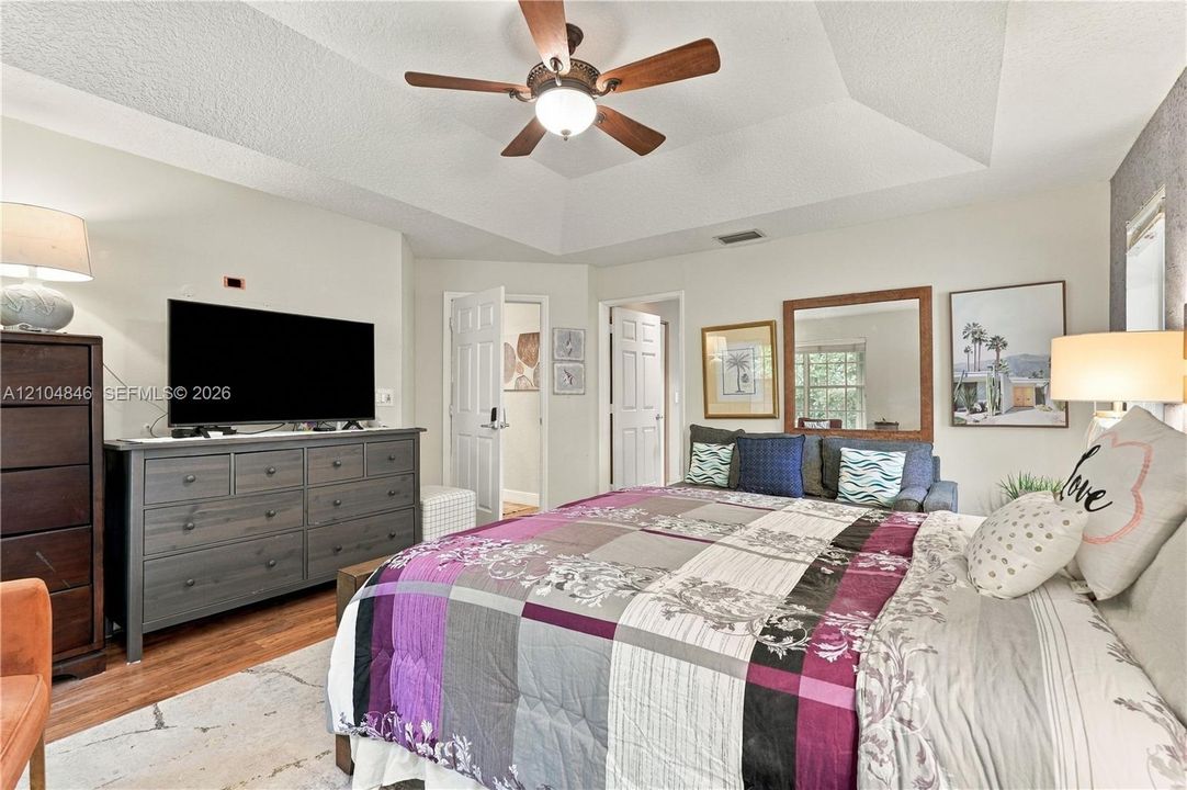 Tray ceiling with a central ceiling fan and wood-finish flooring