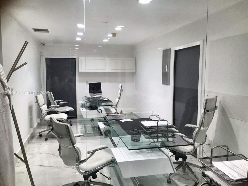 Polished stone flooring, recessed ceiling lighting, wall-mounted upper cabinetry, and glass-partitioned wall enclosure