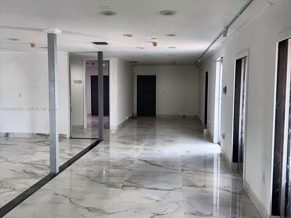 Large-format stone-look tile flooring with grey veining, recessed ceiling lighting, and structural support columns