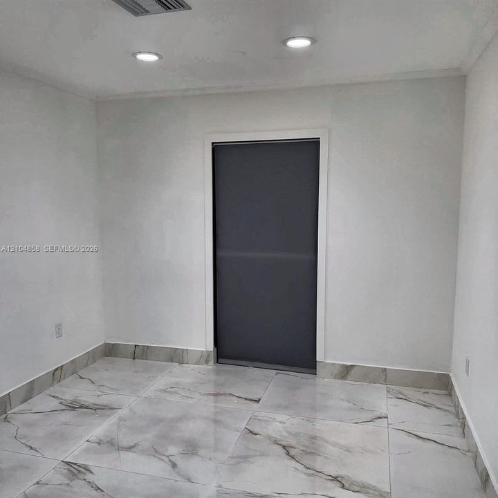 Large-format stone-look floor tiling with matching wall trim, recessed ceiling lighting, and a single-panel interior door