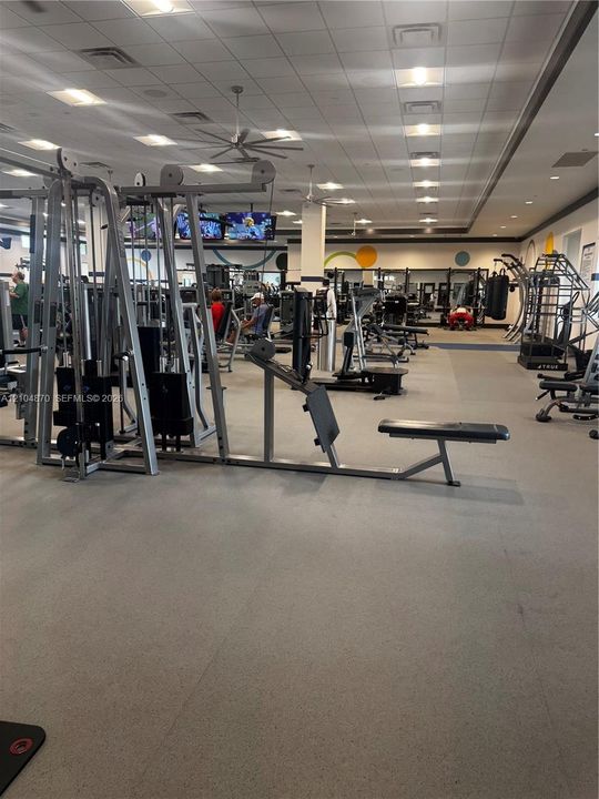 Fitness center featuring a drop ceiling with recessed lighting, ceiling fans, resilient rubber flooring, and full-length wall mirrors