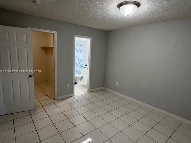 Interior space featuring light-toned ceramic tile flooring, neutral wall paint, a six-panel interior door, and a built-in closet with shelving