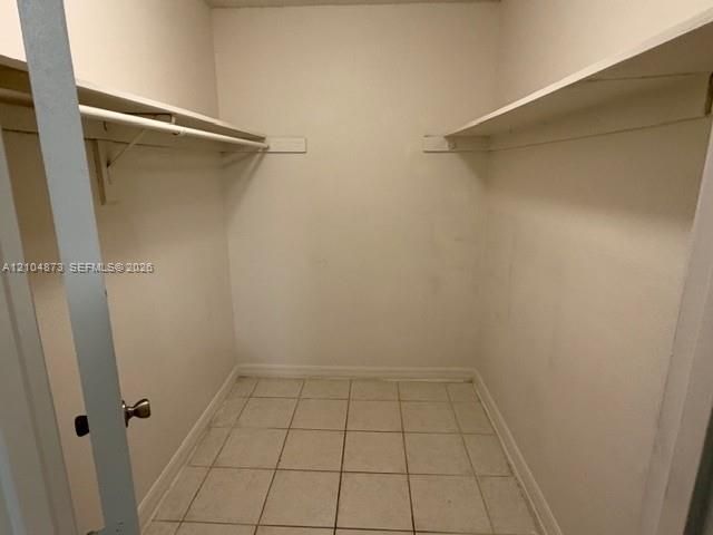 Walk-in storage space featuring ceramic tile flooring, built-in shelving, and mounted garment rods