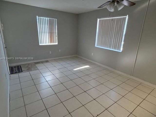 Neutral-toned interior featuring ceramic tile flooring, dual windows with vertical blinds, and a ceiling fan