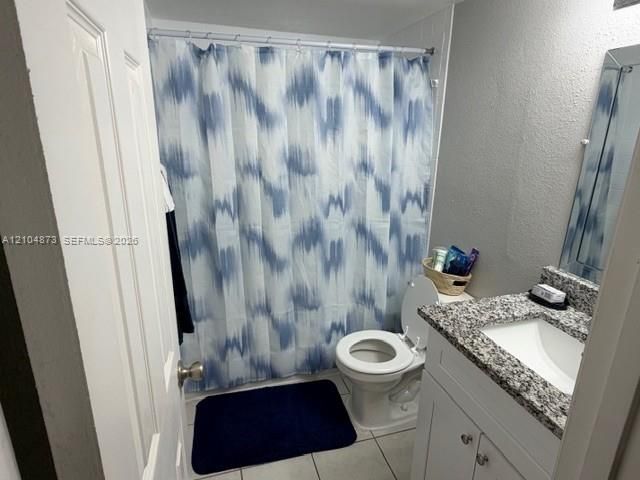White vanity with stone-composite countertop, undermount sink, tiled flooring, and porcelain commode