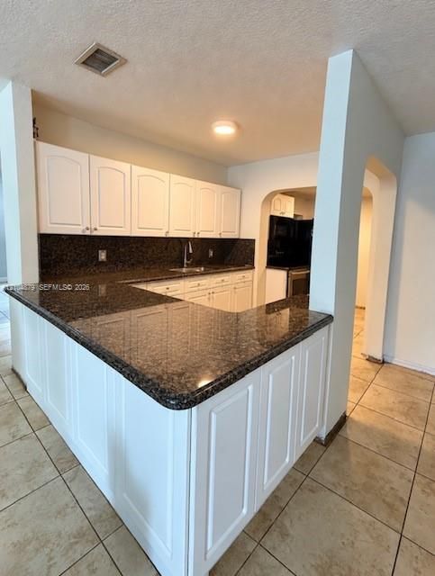 Kitchen featuring white shaker-style cabinetry, dark speckled countertops, a double-basin sink with a chrome faucet, and tile flooring