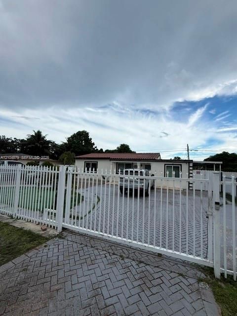 White metal security gate, paver driveway, and a single-story residence with a red tile roof