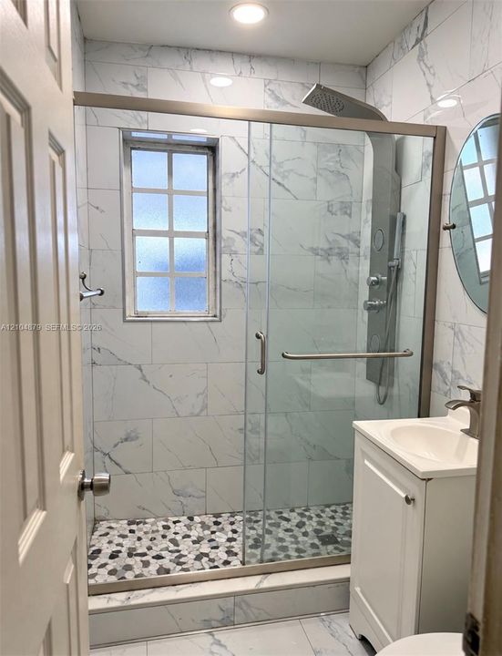 Glass-enclosed shower with pebble-finish flooring, white tile surrounds, and a multi-function shower system