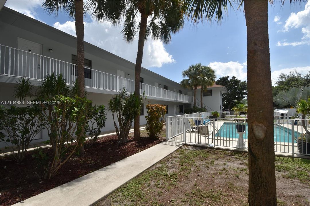 Multi-story building featuring exterior balconies with white railings, a fenced outdoor pool, and mature palm trees