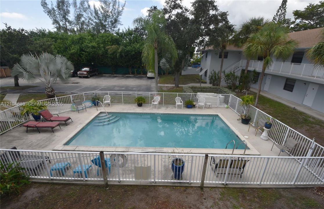Outdoor swimming pool with integrated steps, surrounded by a concrete deck and white aluminum fencing