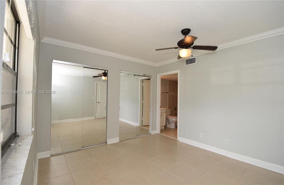 Ceiling fan with integrated lighting, crown molding, tile flooring, mirrored closet doors, and an en-suite bathroom