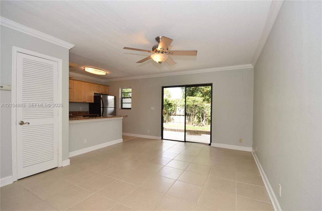 Tiled flooring throughout, crown molding, ceiling fan with integrated lighting, wood cabinetry, and sliding glass door