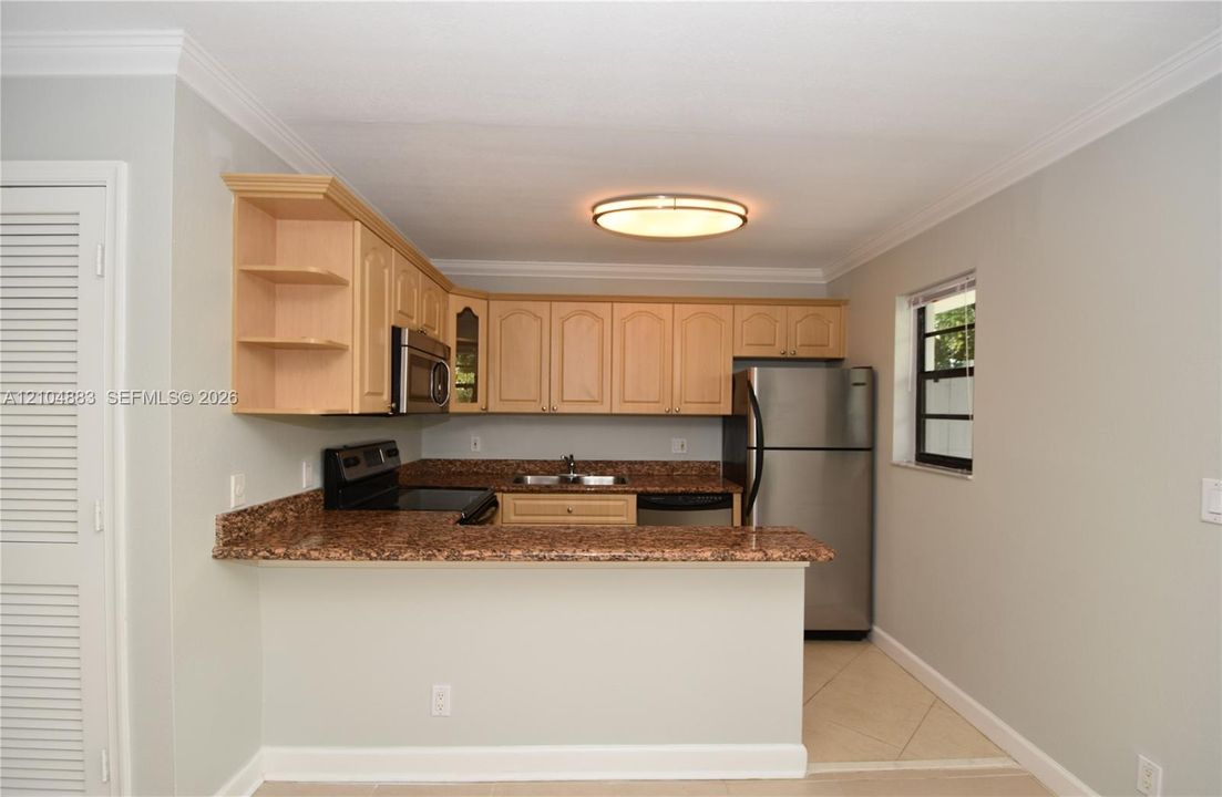 Kitchen featuring light wood cabinetry, stone countertops, stainless steel appliances, and tile flooring