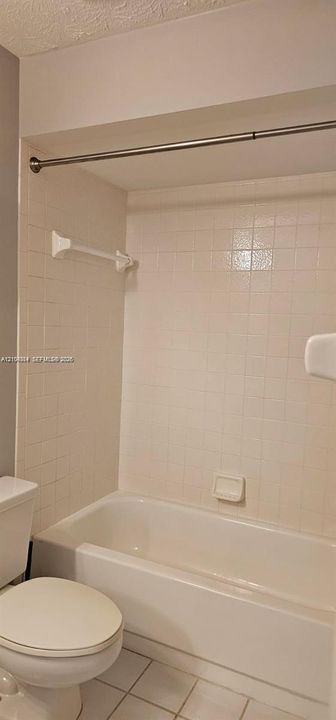 White tiled shower and bathtub combination with a chrome shower rod and white toilet