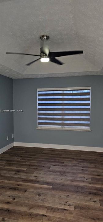 Tray ceiling with a modern ceiling fan, wood-finish flooring, and a large window with horizontal blinds