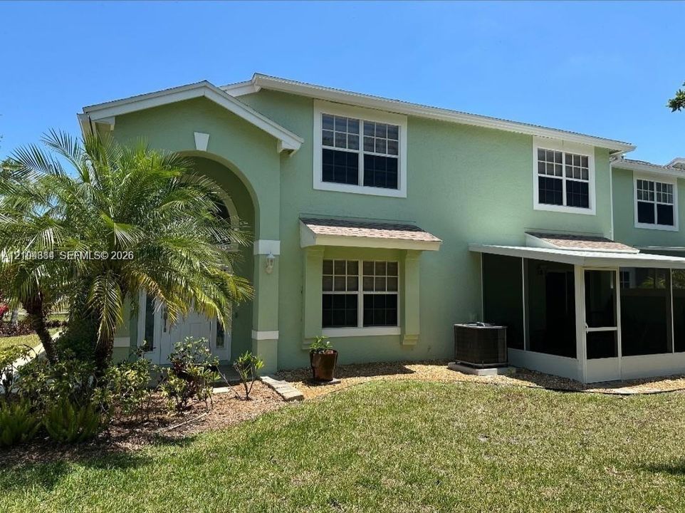 Two-story stucco exterior with an arched entryway, multiple pane windows, a covered screened patio, and a landscaped front yard