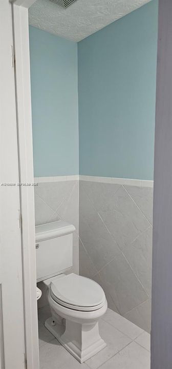 Compact water closet featuring a two-piece toilet, tiled wainscoting, and a tiled floor