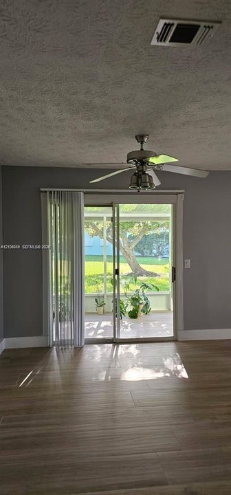 Wood-finish flooring, ceiling fan with integrated lighting, sliding glass doors, vertical window blinds, and an enclosed patio