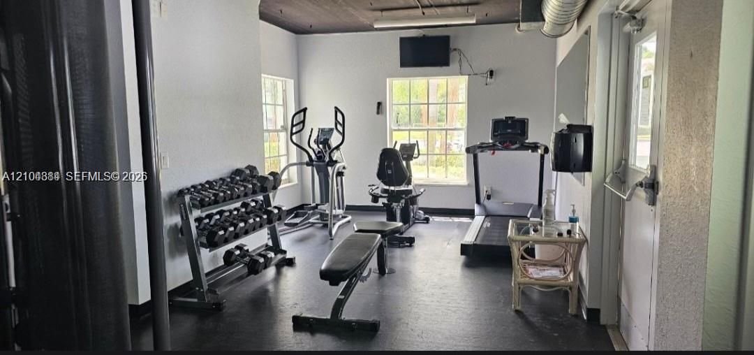 Fitness room with dark resilient flooring, white walls, and multiple windows