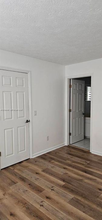 Wood-finish flooring with white baseboards, a textured ceiling, and a paneled door