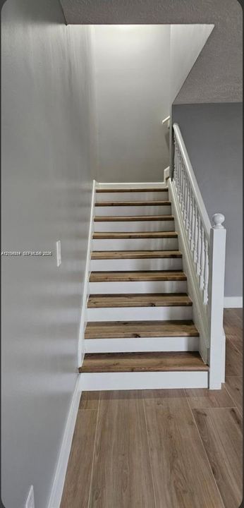 Staircase featuring wood-finish treads and white risers, complemented by a white baluster railing and wood-finish flooring