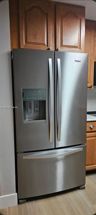 Stainless steel French door refrigerator with integrated ice and water dispenser, complemented by light wood-tone cabinetry and wood-finish flooring